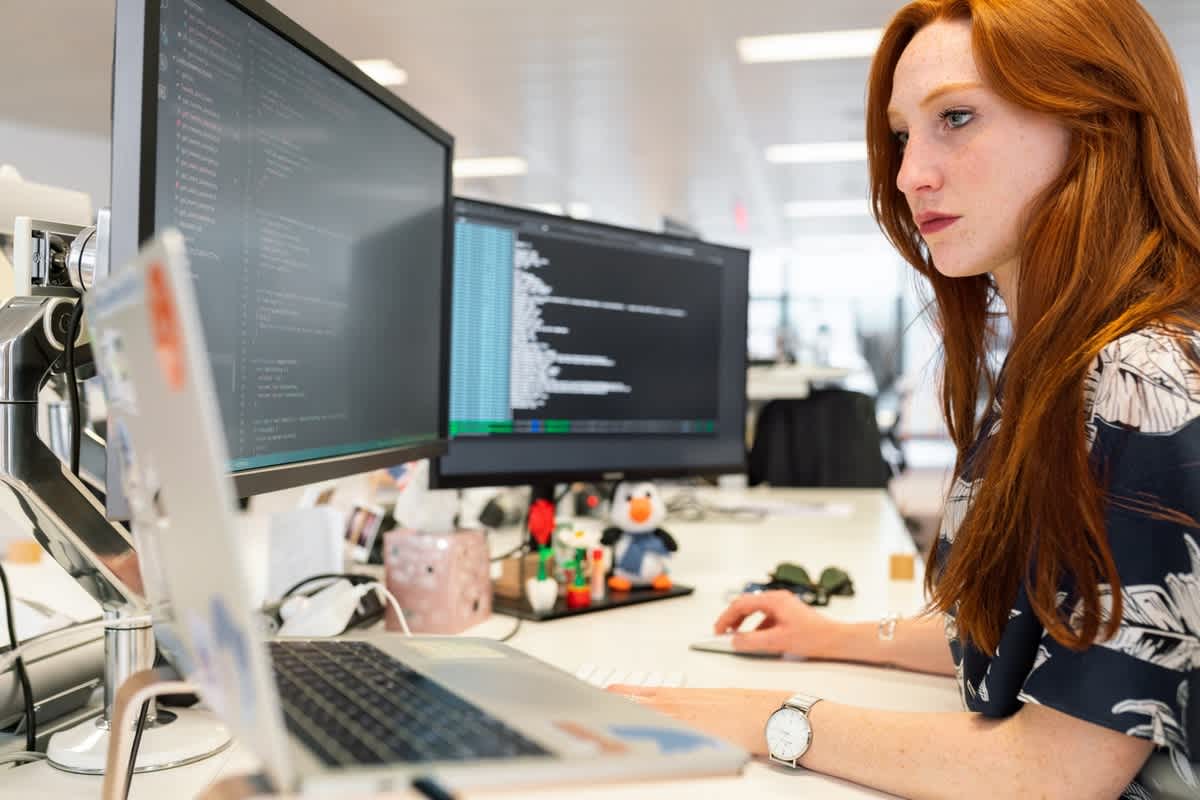 Software developer working with code across a laptop and two monitors